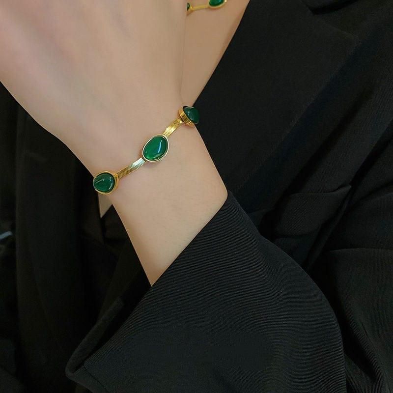 Gold bracelet with green stones on a wrist against a black background