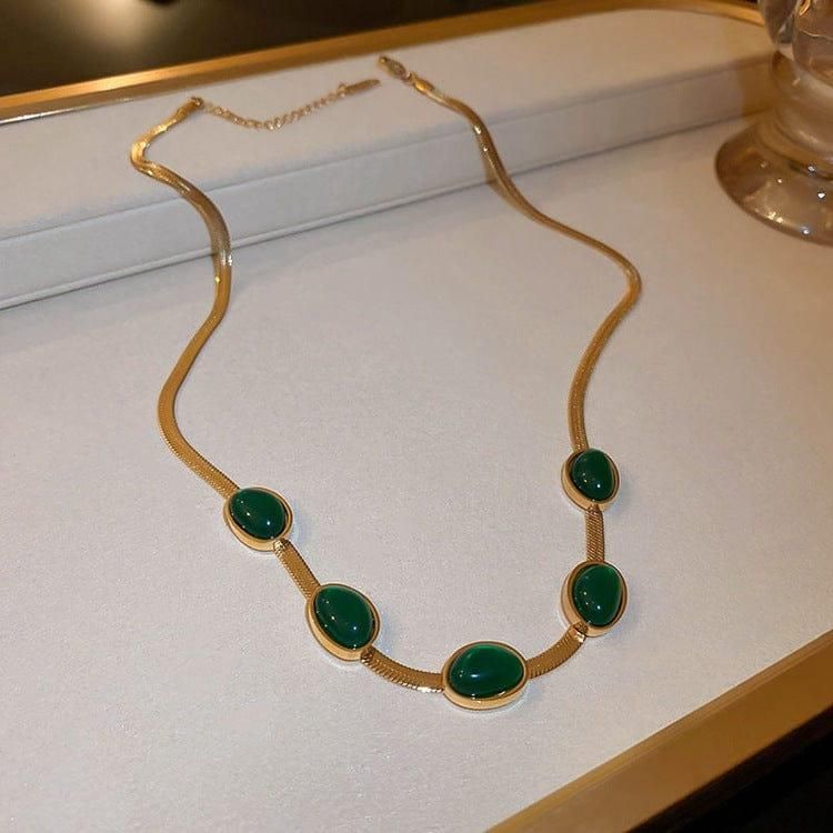 Gold necklace with green stones on a white surface